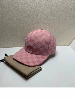 Rosa keps med GG-mönster - Snygg rosa keps med klassiskt GG-mönster i två nyanser av rosa. Kepsen har böjd skärm och justerbart spänne bak i rosa läder. Tillverkad i canvasmaterial med insida i ljus textil. Perfekt för dig som vill sticka ut med en lyxig accessoar.