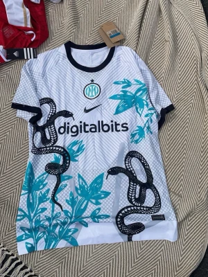 Inter Milan Nike fotbollströja ormmönster - Snygg vit Inter Milan fotbollströja från Nike med svart ormmönster och turkosa bladmönster. 