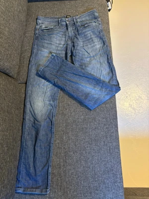 Blå slim fit jeans från BOSS - Snygga blå slim fit jeans från BOSS med klassisk femficksdesign. Jeansen har normal midja, dragkedjegylf och är tillverkade i ett mjukt denimtyg som ger en bekväm känsla. Perfekta för en avslappnad och trendig look. Priset går att diskutera, säljer dessa då de är försmå för mig. 31/32