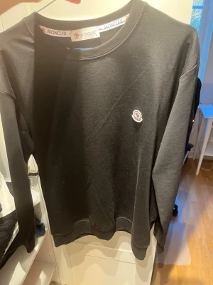 Svart långärmad topp från Moncler - Svart långärmad topp från Moncler med rund halsringning och diskret Moncler-logga på bröstet. Tillverkad i mjukt material som känns skönt mot huden. Enkel och stilren design som passar till många olika outfits. Fler bilder kan skickas vid förfrågan!👍