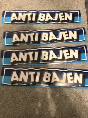 Blåa klistermärken med text 'ANTI BAJEN' - Fyra rektangulära klistermärken i blåa nyanser med vit och svart text 'ANTI BAJEN'. Klistermärkena har en grafisk stil med tydliga konturer och är gjorda av plastmaterial. Perfekt för att dekorera till exempel laptop, väska eller andra ytor.