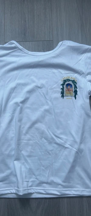 Vit t-shirt från Casablanca - Vit t-shirt från Casablanca med tryck av en byggnad och texten 'CASABLANCA AVENIDA' på bröstet och ryggen. Klassisk passform med rund hals och korta ärmar. Perfekt för en chill och stilren look. Storleken är M men skulle säga att den sitter mer som S. Aldrig använd! 
