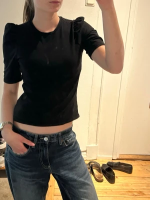 Svart topp med puffärm - Trendig svart topp med puffärmar och rund hals. Modellen är croppad och har en tight passform som framhäver midjan. Perfekt att styla med jeans eller kjol för en cool look.