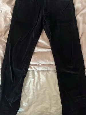 Svarta manchesterbyxor från Wrangler 32/30 - Svarta manchesterbyxor från Wrangler med klassisk femficksdesign och raka ben. Byxorna har tydliga sömmar på bakfickorna och bälteshällor i midjan. Perfekta för dig som gillar en tidlös och avslappnad stil.