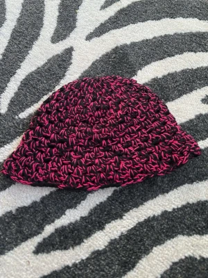 Handvirkad svart och rosa bucket hat - Unik handvirkad bucket hat i svart och rosa  bomullsgarn. Sitter bra på mig som har 55 i omkrets på huvudet.