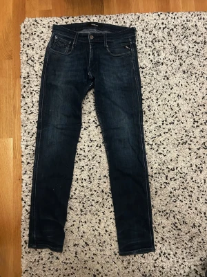 Mörkblå slim fit jeans från replay  - Snygga mörkblå slim fit jeans från replay med klassisk femficksdesign och diskreta slitningar. Jeansen har smal passform och är tillverkade i stretchigt denimtyg för extra komfort. Perfekta för en trendig och avslappnad look.