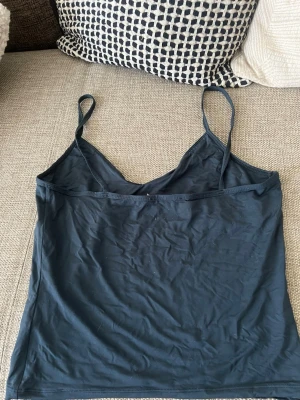 Marinblå linnetopp med smala axelband - En enkel och stilren marinblå linnetopp med smala axelband och v-ringad halsringning. Perfekt att matcha med jeans eller kjol för en avslappnad look. Tunt och mjukt material som känns skönt mot huden.