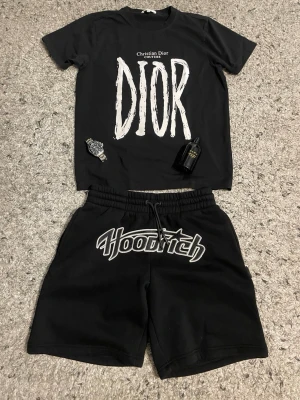 Svarta Hoodrich shorts  - Svarta shorts från Hoodrich med stor broderad logga framtill i vitt och grått. Modellen har elastisk midja med snörning för skön passform. Perfekta för en avslappnad streetwear-look.