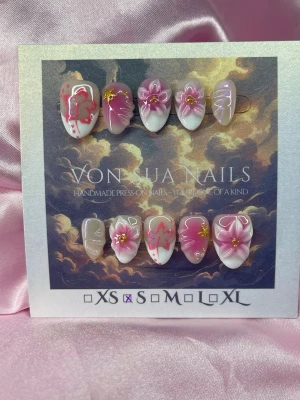 SakuraPetals (S);Short Almond - Handgjorda press-on naglar i rosa och vitt med blommönster, 3D-detaljer och små guldfärgade accenter. Naglarna har en kort almond form och är dekorerade med både målade och handgjorda blommor. Perfekt för dig som vill ha unika och kreativa naglar.S: 15 mm, 11,5 mm, 12 mm, 11 mm, 9 mm 