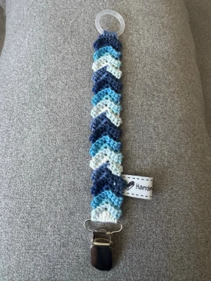 Virkad napphållare - Virkad napphållare i blåa nyanser. Virkad av mig i 100% bomullsgarn med metallclip och silikonring.  Mönsterskapare: animo.design