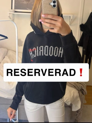 (RESERVERAD) - Cool svart hoodie från Hoodrich i en med stor logga på bröstet och detaljer i rött. Har huva och känguruficka framtill. Texttryck på ryggen/vänster handled och broderade detaljer på huvan. Perfekt för dig som gillar streetwear och vill ha något unikt!