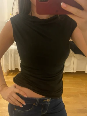 Svart ärmlös topp i bomull - Snygg svart topp med hög hals och ärmlös design. Tillverkad i mjuk bomull som sitter tight mot kroppen och ger en clean look. Perfekt att matcha med jeans eller kjol för en enkel men stilren outfit.