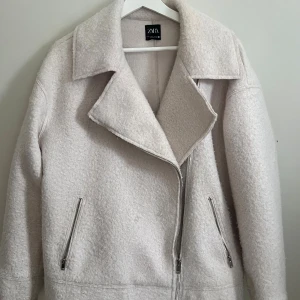 Vår jacka  - Snygg vit jacka från Zara i ullmix med stor krage och asymmetrisk dragkedja framtill. Jackan har två fickor med silverfärgade dragkedjor och en mjuk, lite fluffig yta. Perfekt för kyligare dagar och enkel att styla till olika outfits.