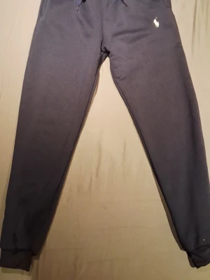 Mörkblå mjukisbyxor från Polo Ralph Lauren - Mörkblå mjukisbyxor från Polo Ralph Lauren med klassisk logga broderad på vänster höft. Byxorna har dragsko i midjan och muddar vid bensluten. Perfekta för en avslappnad och stilren look.