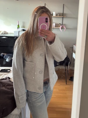 Ljusgrå kappa - Snygg ljusgrå kappa med stora knappar framtill. Kappan har två fickor. Storlek xs den är från lager 157 och är oanvänd.