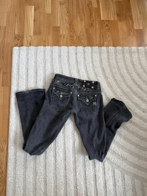 Gråa Miss Me jeans med paljettdetaljer - Snygga grå jeans från Miss Me med raka ben och coola paljettdetaljer i zebramönster på bakfickorna. Dekorativa nitar och tydliga sömmar ger extra attityd. Perfekta för dig som vill sticka ut lite extra!