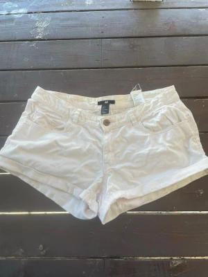 Ljusrosa shorts från H&M med fickor - Säljer ett par ljusrosa shorts från H&M med klassisk femficksdesign och knappgylf. De har upprullade benslut och är tillverkade i mjuk bomull, perfekta för varma dagar. Passar dig som gillar en enkel och clean stil.