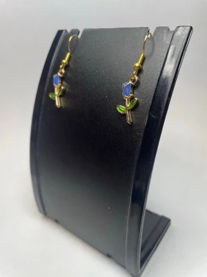 Blå rosörhängen med gulddetaljer - Snygga örhängen i form av blå rosor med guldfärgade krokar och detaljer. Rosorna har gröna blad och stjälk, vilket ger en färgglad och lekfull look. Perfekta för dig som vill ha något unikt och sött till din stil.