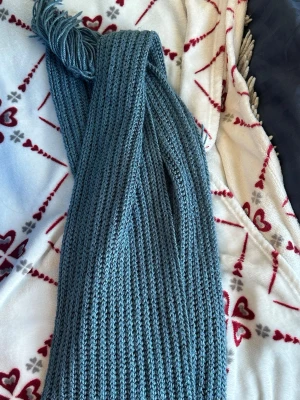 Blå ribbstickad halsduk med fransar - Säljer en lång, ribbstickad halsduk i en snygg blå nyans. Halsduken har fransar i ändarna och är gjord i ett mjukt, stickat material som känns skönt mot huden. Perfekt accessoar för att lyfta din outfit under kyliga dagar.