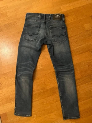 Blå jeans från Replay - Säljer ett par snygga blå jeans från Replay i anbass (slim fit) med klassisk femficksdesign. Jeansen ha en mörk tvätt med ljusare partier. Storlek W29 L30