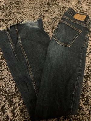 Mörkblå jeans med råa benslut 157 - Snygga mörkblå jeans från 157 med raka ben och trendiga råa benslut. Klassisk femficksmodell med dragkedja och knapp. Jeansen har kontrastsömmar och är tillverkade i denim med lite stretch för skön passform.