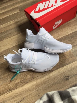 Nike Presto vita sneakers - Nike Presto sneakers i helvit färg med mesh-överdel och plastdetaljer vid snörningen. Skorna har en sportig och clean design med rund tå och tjock sula. Perfekta för dig som gillar stilrena och bekväma sneakers.