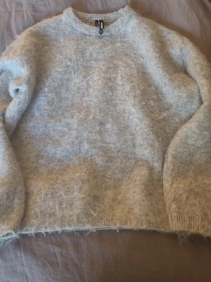 Ljusgrå fluffig stickad tröja Bik Bok - Mysig ljusgrå stickad tröja från Bik Bok med fluffig yta. Tröjan har rund halsringning, långa ärmar och ribbade muddar. Tröjan är dock något stickig och rekommenderar därför att ha ett linne under.