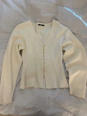 Vit kofta från Gina Tricot - Säljer en stilren vit kofta från Gina Tricot med v-ringning och dekorativa knappar framtill. Koftan har lång ärm och är gjord i ett mjukt, tunt stickat material som passar perfekt till lager på lager. Enkel och clean design som är lätt att matcha.