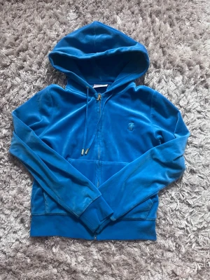Blå velour hoodie från Juicy Couture - Snygg blå hoodie i mjuk velour från Juicy Couture. Dragkedja framtill, fickor och justerbar huva med snören. Ikonisk JC-logga broderad på bröstet. Perfekt för en chill och trendig look. Går inte att köpa längre därav priset 🤍 båda grejerna på snörena är kvar och tröjan är i nyskick 🤍