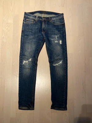 Nudie Jeans  - Tjena! Säljer nu dessa nudie jeans med en sjukt snygg tvätt samt slitningar. Storlek 34/32 och i väldigt bra skick. Priset är ej hugget i sten så hör av dig vid minsta fundering:)