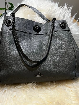 Grå Coach väska - Grå coach väska som jag använt såpass lite så jag säljer den, den har en liten fläck inuti som man ser på bilden och ytterst lite av något rosa som knappt syns.