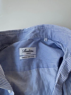 Blårandig skjorta från Stenströms - Snygg blårandig skjorta från Stenströms i modellen Slimline. Tillverkad i tvåfaldigt super bomullstyg som känns lyxigt och mjukt. Skjortan har klassisk krage, långa ärmar och knappar framtill. Skriv ifall du har några frågor!