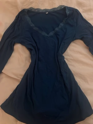 Blå långärmad topp med spets - Blå långärmad topp med v-ringning och dekorativ spetskant runt halsen. Toppen har en smickrande passform och är tillverkad i ett mjukt material som känns skönt mot huden. Perfekt för dig som gillar stilrena detaljer.