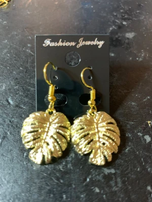 Guldiga örhängen med monstera-blad - Snygga örhängen i guldfärgad metall formade som monstera-blad. De har en krok för enkel användning och ger en trendig touch till din stil. Perfekta för dig som gillar statement-smycken och naturinspirerad design.