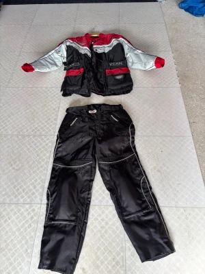 MC-ställ VCAN svart/röd/vit - Säljer ett MC-ställ från VCAN med jacka och byxor i slitstarkt syntetmaterial. Jackan är svart, röd och vit med flera fickor, justerbara band i midjan och dragkedja. Byxorna är svarta med vita detaljer och förstärkningar vid knän och höfter. Perfekt för motorcykelåkning.  CE märkt