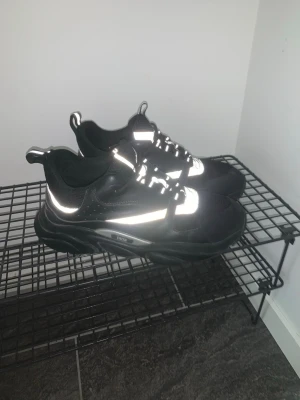 Dior b22 storlek 43 - Stilrena svarta chunky sneakers med feta sulor och reflekterande detaljer på ovandelen. Skorna har snörning och dragflikar både fram och bak för enkel påtagning. Perfekta för dig som gillar streetwear och vill sticka ut lite extra.
