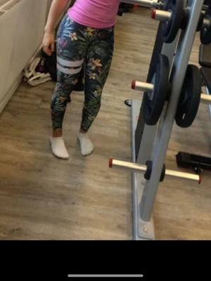  Träningstights från Stronger - Snygga träningstights med tropiskt blommönster i grönt, gult, rosa och vitt. De har två vita ränder på ena benet och bred vit linning. Perfekta för gymmet eller träning, sitter tight och är gjorda i stretchigt syntetmaterial. Litet litet hål vid midjan, se sista bild 