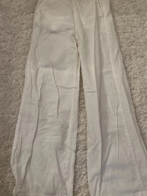 Vita  linnebyxor - Säljer ett par vita linnebyxor med avslappnad passform och resår i midjan. Byxorna har raka, vida ben och är tillverkade i ett lätt och luftigt linnetyg. 