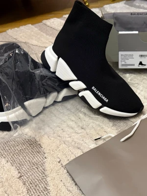 Balenciaga Speed Trainer svarta sneakers - Svarta Balenciaga Speed Trainer sneakers med vit chunky sula och stickad sock-liknande ovandel. Logotypen är tryckt på sidan. Skorna har en modern och sportig design med elastiskt material som formar sig efter foten.