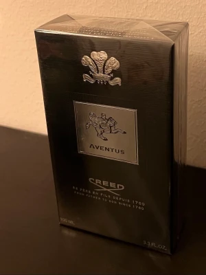 Creed Aventus Eau de Parfum 100 ml - Lyxig parfym från Creed, Aventus, i en elegant svart och silverfärgad förpackning. Flaskan rymmer 100 ml och har exklusiva detaljer med silveremblem och klassisk design. Aventus är känd för sin unika doftprofil och ikoniska status inom parfymvärlden.