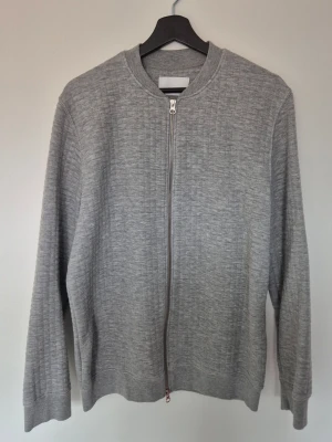 Samsøe Samsøe Grå ziptröja i bomullsmix - Snygg grå ziptröja med diskret rutstruktur och rund hals. Tröjan har dragkedja framtill, långa ärmar och ribbade muddar. Perfekt att slänga på sig över en t-shirt för en clean och enkel look.