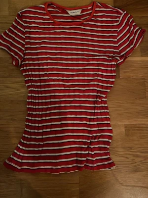 Rödvit randig t-shirt från Gant - Säljer en röd och vit randig t-shirt från Gant med rund halsringning och korta ärmar. T-shirten har en figurnära passform och är gjord i mjuk bomull. Perfekt för en avslappnad och stilren look.