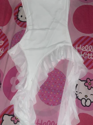 Vit tröja med volangdetaljer - Snygg vit tröja med transparenta volangdetaljer i mesh längs sidorna. Kroppsnära passform och högt skuren vid benen. Perfekt för dig som vill ha något unikt och trendigt i garderoben.