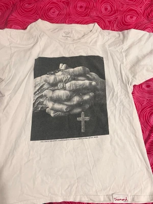 Vit Diamond t-shirt - Vit t-shirt från Diamond Supply Co med ett stort svartvitt tryck av händer med ringar och ett kors på framsidan. Texten 'ALL HOLY TRINITY, HAVE MERCY ON ME, LORD, FORGIVE MY SINS.' 