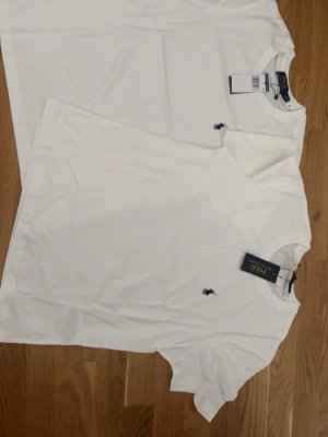 Vit t-shirt från Polo Ralph Lauren - Klassisk vit t-shirt från Polo Ralph Lauren med korta ärmar och rund hals. T-shirten har den ikoniska broderade loggan på bröstet och är tillverkad i mjuk bomull för en skön känsla. Perfekt basplagg till garderoben.