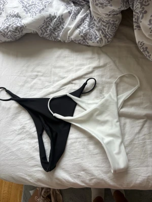 Svart och vit bikiniunderdel - Två string bikiniunderdelar i svart och vitt med enkel, smal design och tunna band i sidorna. Perfekta för sommaren och strandhäng. Materialet känns mjukt och stretchigt, vilket ger en bekväm passform.
