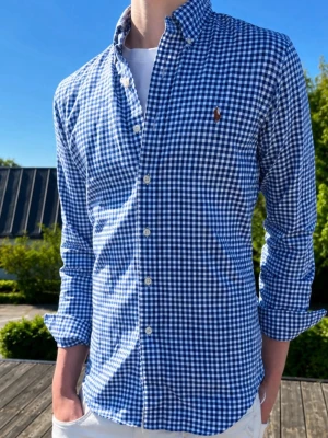 Blårutig skjorta från Ralph Lauren - Vit blå rutig (MODELLEN ÄR 185CM OCH VÄGER 75KG)Klassisk blårutig skjorta från Ralph Lauren med button-down krage och broderad logga på bröstet. Skjortan har lång ärm, vita knappar och är tillverkad i mjuk bomull. Perfekt för en avslappnad men ändå stilren look.