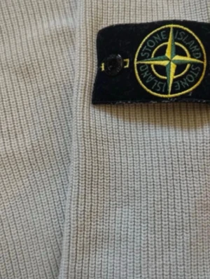 Stone Island- Ice white sweater - Snygg beige stickad tröja från Stone Island med klassisk patch på ärmen och ribbstickad rund hals. Perfekt för dig som gillar streetwear och vill ha något stilrent men ändå trendigt.