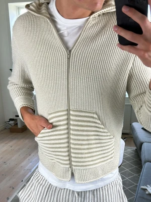 Unik beige randig hoodie  - Snygg, beige och stickad hoodie med tunna horisontella ränder och dragkedja framtill. Väldigt trendig och perfekt under sommarkvällarna! Mått: A:41 B:44 C:38 D:61 (cm)  Skriv vid fundering😇✌️