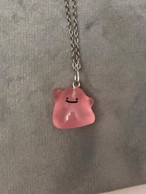 Självlysande Ditto halsband Pokémon smycke  - Så gulligt halsband med en berlock av Ditto!Berlocken är ca 1,5 x 1,5 cm och trädd på en kedja i silverimitation, justerbar 40-45 cm. Betlocken är också självlysande och lyser i mörkret.